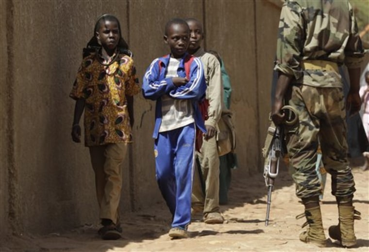 Schoolchildren walk past a soldier guarding the entrance to an army camp where members of Niger's ruling military junta were meeting in Niamey, Niger, on Monday. 
